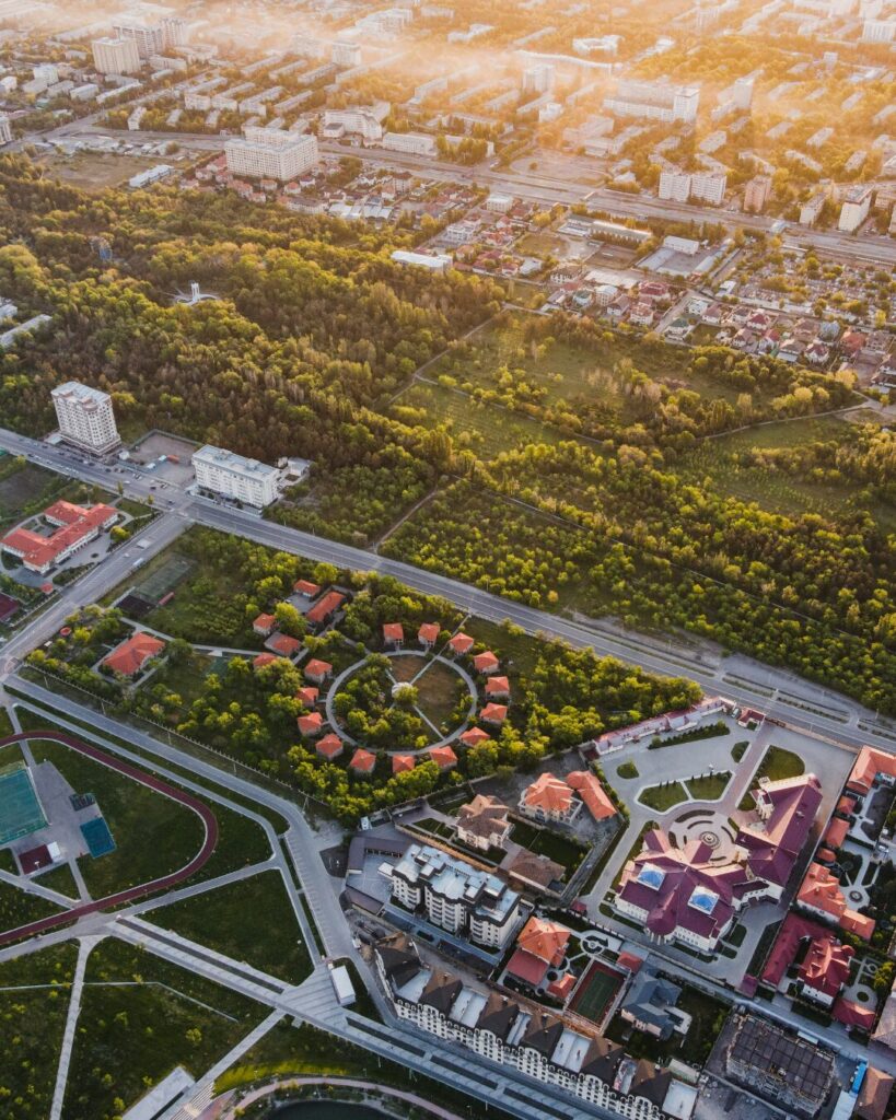 Vista a nivel de calle de un parque público moderno en una zona residencial consolidada, con senderos pavimentados, familias paseando y vegetación cuidada que rodea edificios de viviendas contemporáneos.