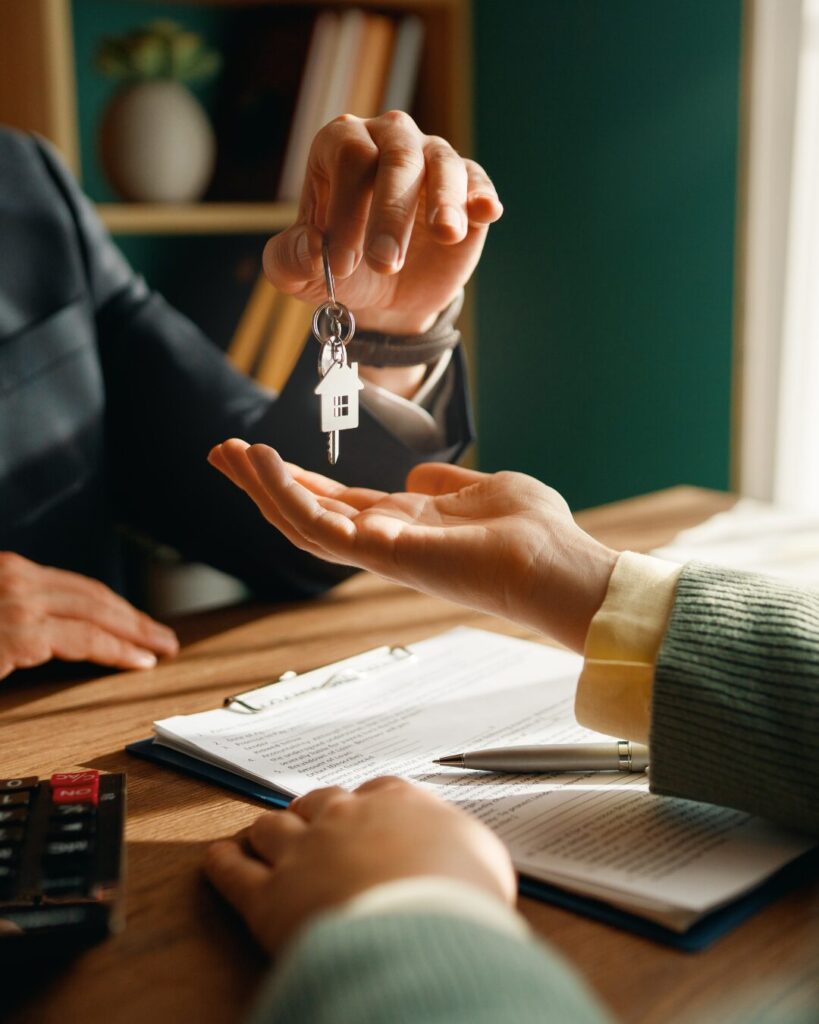 Primer plano de una conversación profesional entre una asesora inmobiliaria y un cliente; se muestran manos señalando puntos clave en un dossier informativo sobre una mesa de madera en una oficina luminosa.